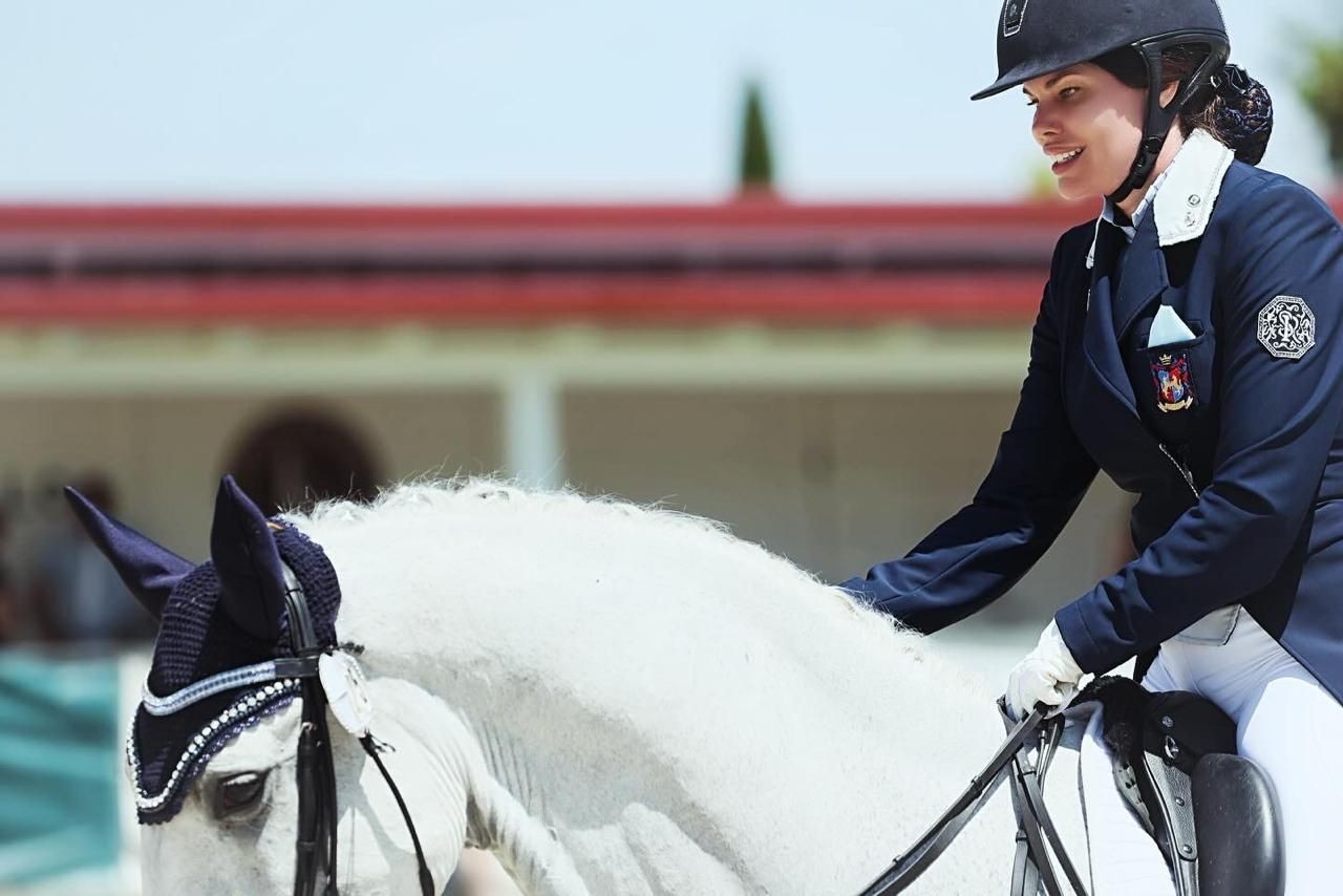 Equestrian rider in uniform riding a white horse during a dressage event.